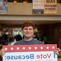 Student holding sign titled "I vote because: I want to have a say in how my country is run"